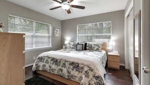 A bedroom with a bed, a nightstand, a ceiling fan, and two windows with blinds.