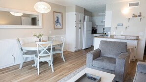 A modern living room with a dining area, a gray armchair, and a kitchen in the background.