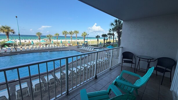 A balcony with a pool, chairs, and a view of the beach and ocean.