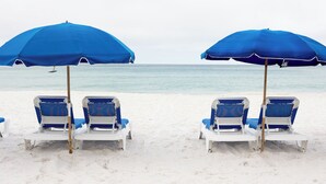 A beach with two rows of blue beach chairs under large blue umbrellas, facing the ocean.