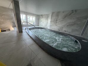 A spa area with a hot tub, marble walls, and a view of the outside.