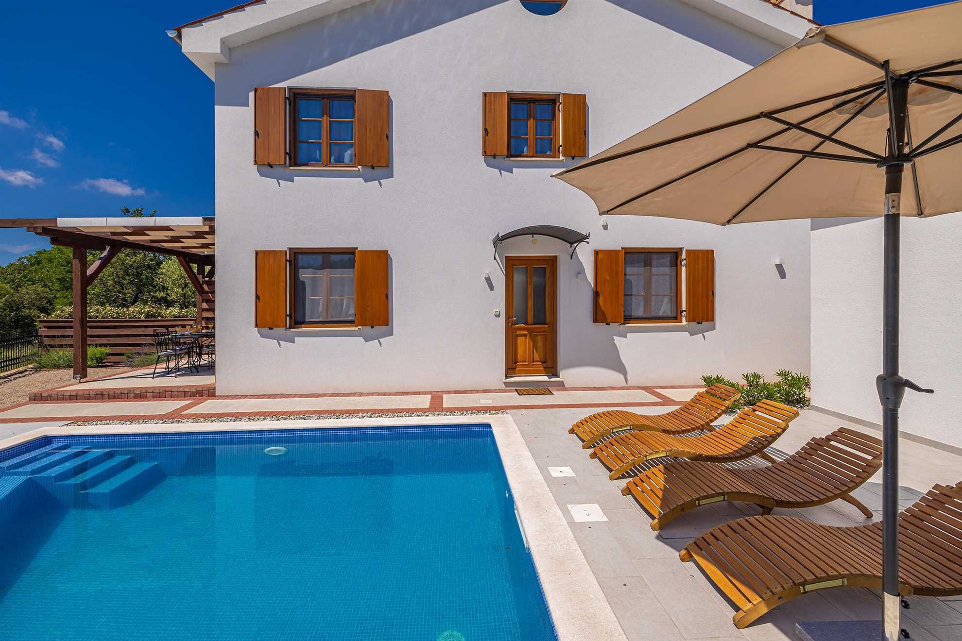 A two-story house with a swimming pool, wooden shutters, and outdoor seating.