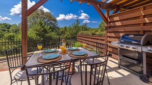 Eine Terrasse im Freien mit einem Tisch für vier Personen, umgeben von Metallstühlen, einem Grill und einem Holzzaun.