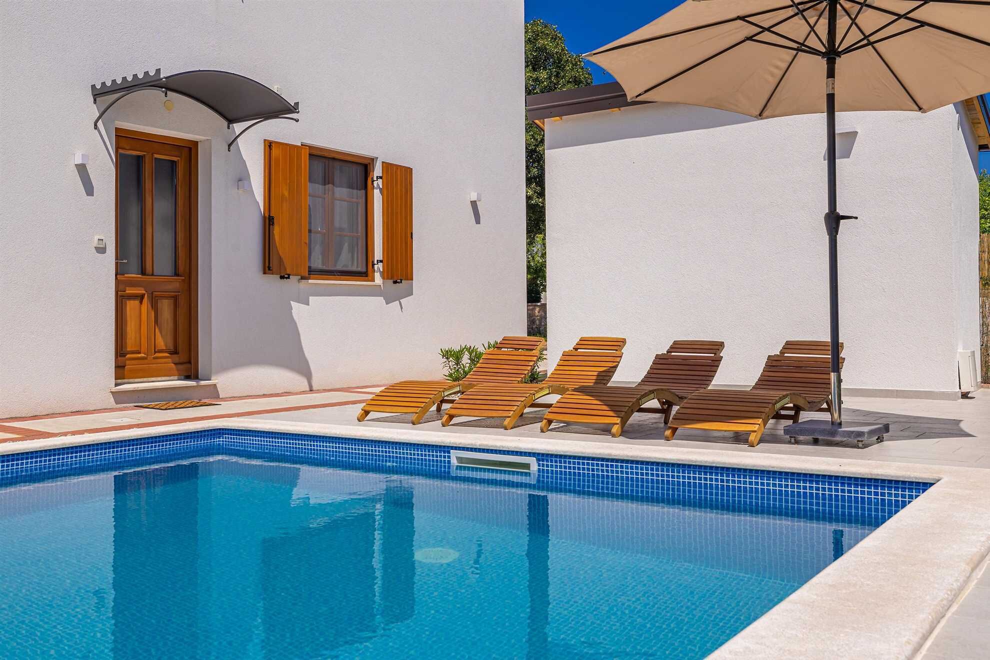A pool area with wooden loungers and a large umbrella.