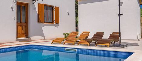 A pool area with wooden loungers and a large umbrella.