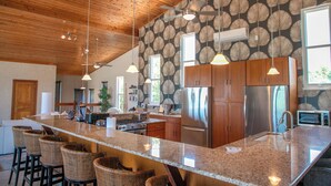 A kitchen with a large island, stainless steel appliances, and a wooden ceiling.