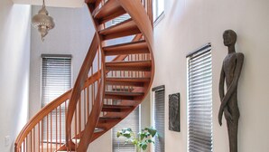 A spiral staircase with wooden railings, a potted plant, and a statue on the wall.