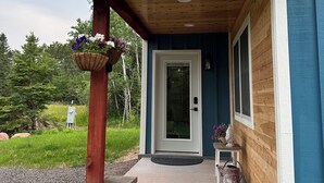Katettu kuisti, jossa on puinen katto, betoniportaat, jotka johtavat ovelle, ja pieni pöytä, jonka päällä on ruukussa oleva kasvi.