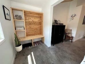 Une pièce comprenant un banc en bois, une armoire noire, une chaise, une décoration murale représentant un crâne de cerf et une plante en pot.