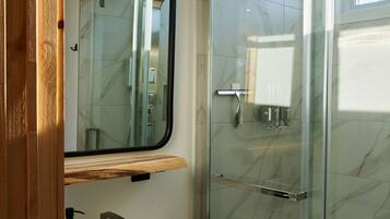 Une salle de bain moderne avec une douche à parois de verre, un lavabo blanc doté d’un distributeur de savon noir et un meuble-lavabo en bois.