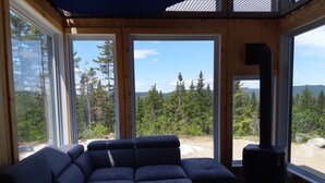 Una habitación acogedora con un amplio sofá modular, una chimenea y grandes ventanales con vistas a un paisaje boscoso.