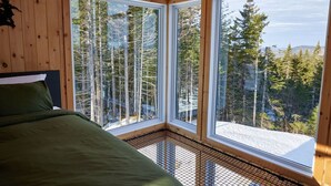 Un dormitorio con un amplio ventanal que ofrece vistas a altos árboles y un paisaje nevado.