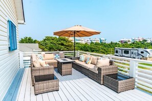 A deck with wicker furniture, an umbrella, and a view of a trailer park. - Barefoot Beach: Spectacular Family Beach Retreat! (Atlantic Beach)
