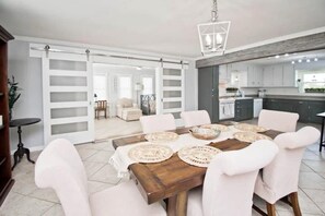 A dining area with a wooden table, white chairs, and woven placemats. - Barefoot Beach: Spectacular Family Beach Retreat! (Atlantic Beach)