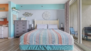 A bedroom with a bed, a dresser, a nightstand, a wall decoration, and a view through a sliding door.