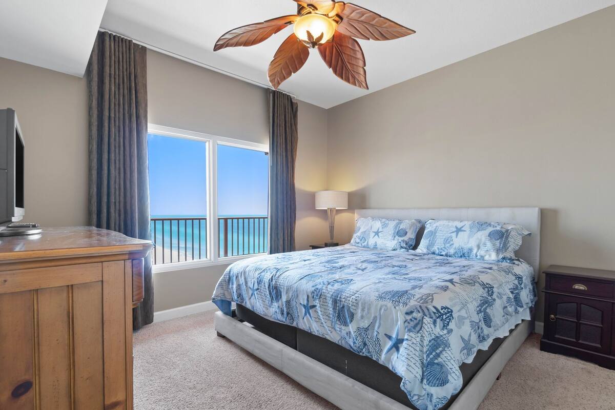 A bedroom with a bed, a desk, a lamp, and a ceiling fan.