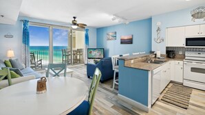 A modern kitchen with a dining area, a TV, and a view of the ocean.