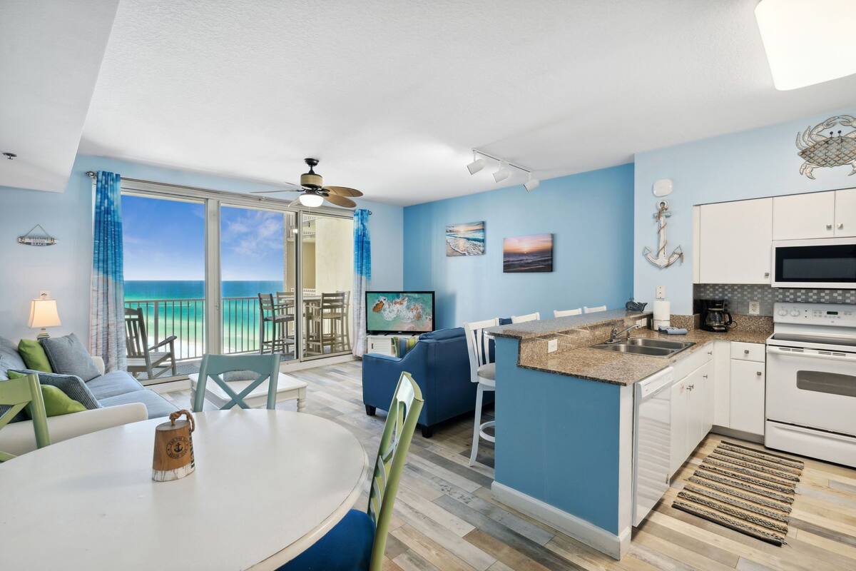 A modern kitchen with a dining area, a TV, and a view of the ocean.