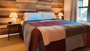 Ein Schlafzimmer mit Wandverkleidung aus Holz, einem Bett mit Tagesdecke, zwei Nachttischlampen und einem Fenster mit Vorhängen.