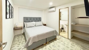 A bedroom with a bed, bedside tables, a wardrobe, and a bathroom with a sink and toilet. - Casa de la Belleza, Uniquely designed 7 bedroom home (Cartagena de Indias)