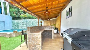 An outdoor kitchen area with a stone countertop, a grill, and a seating area with a chair. - Casa de la Belleza, Uniquely designed 7 bedroom home (Cartagena de Indias)