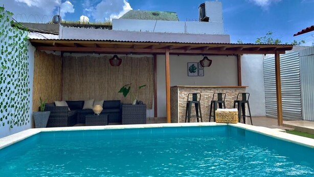 A swimming pool with a covered seating area, a bar, and a thatched wall. - Casa de la Belleza, Uniquely designed 7 bedroom home (Cartagena de Indias)
