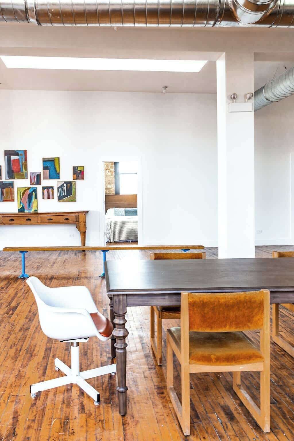 A conference room with a long table, wooden chairs, a white office chair, and a wall with abstract paintings.