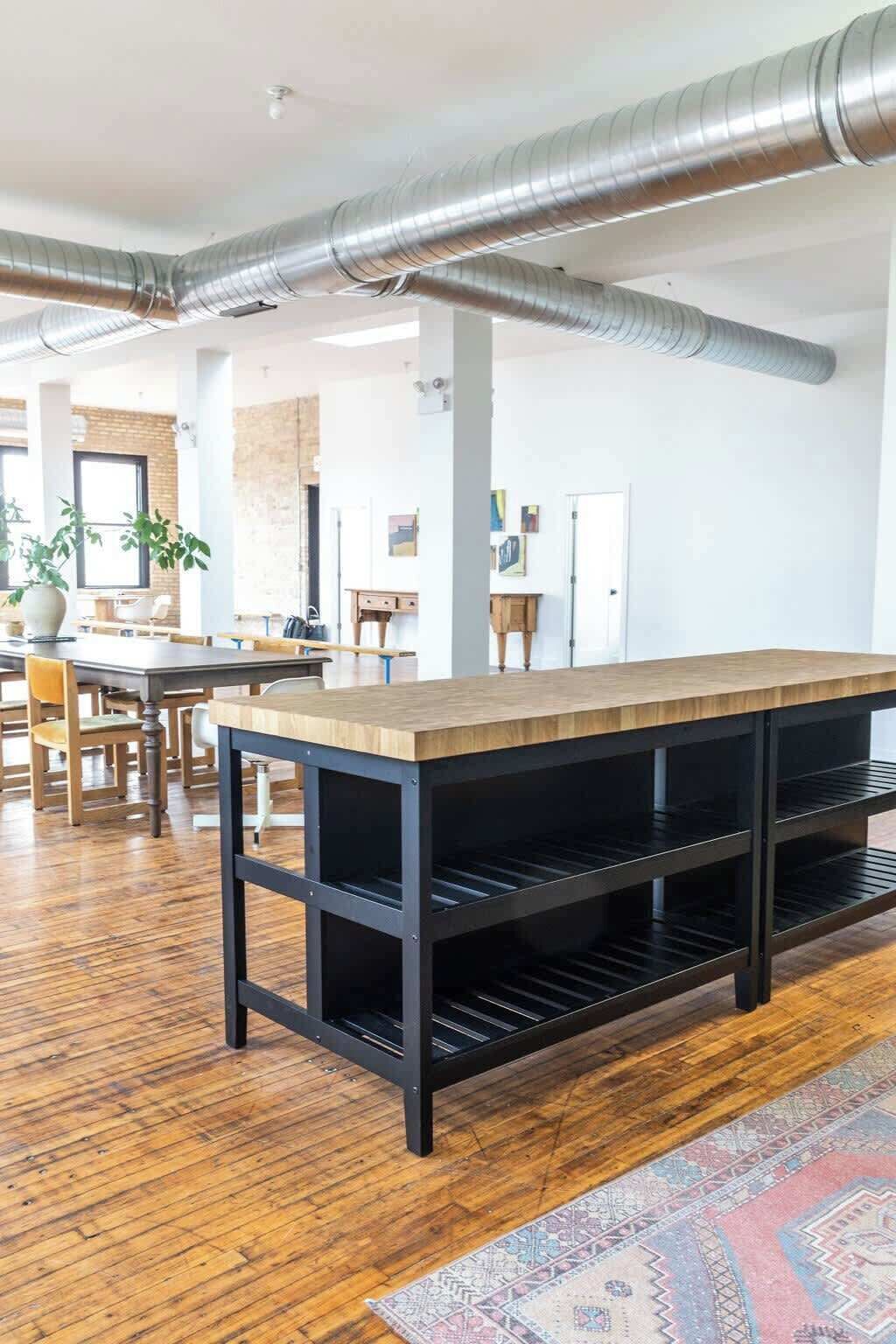 Une pièce spacieuse avec une longue table en bois, des étagères noires et des conduits apparents au plafond.