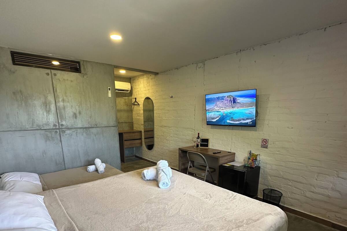 A hotel room with a large bed, a TV mounted on the wall, a small desk, and a mirror.
