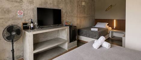 Een moderne hotelkamer met een flatscreen televisie, een minibar, een bed met een grijze plaid en een nachtkastje.