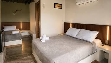 Habitación de hotel con una cama grande, dos mesitas de noche, aire acondicionado de pared y techo con vigas a la vista.