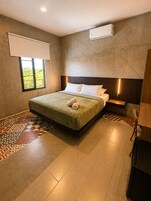 A hotel room with a bed, a window with a view, a wall-mounted air conditioner, and a patterned floor.