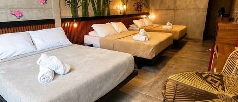 A hotel room with a large bed, two smaller beds, a seating area with wicker chairs, and a wall mural.