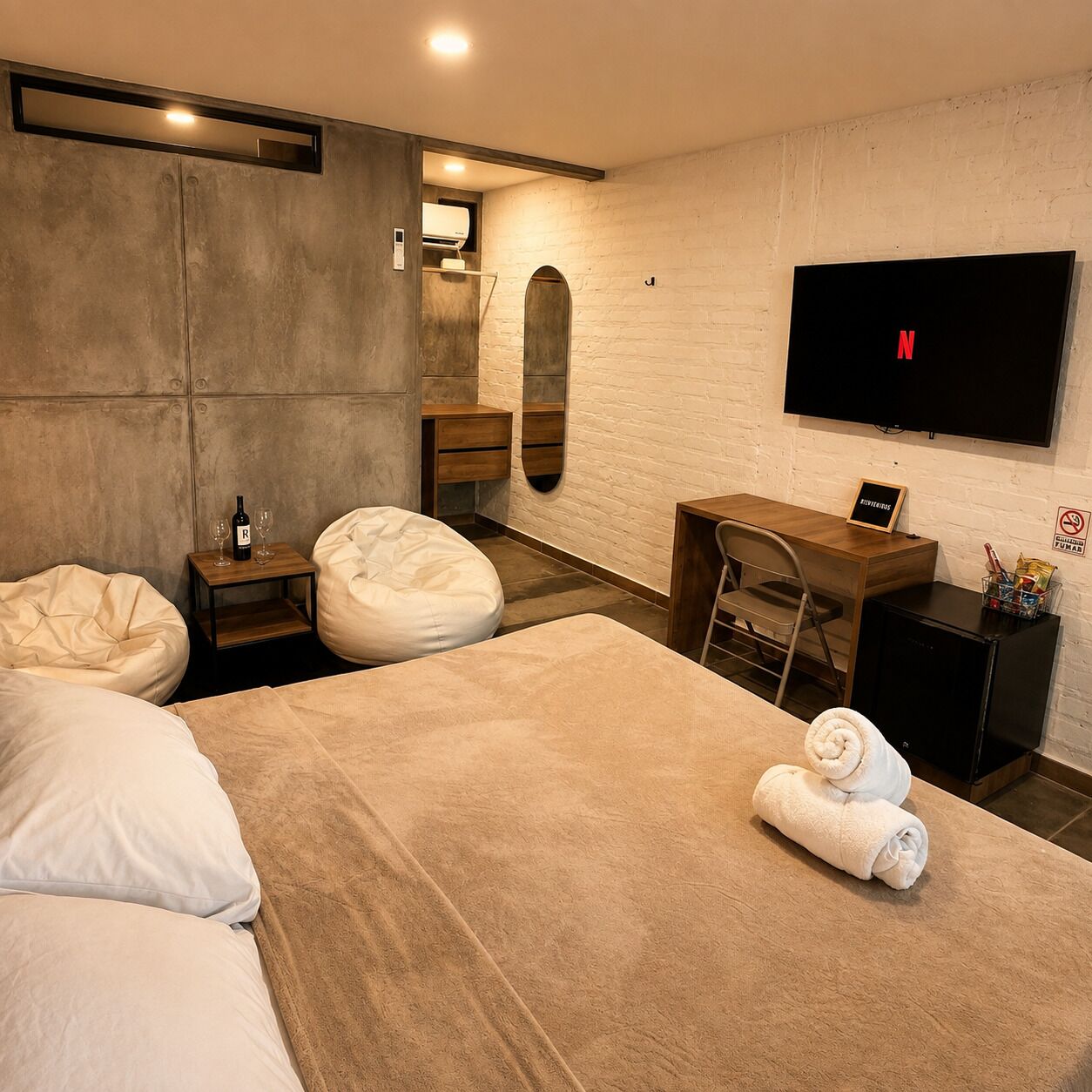 A modern hotel room with a large bed, two bean bags, a desk, a TV, and a minibar.
