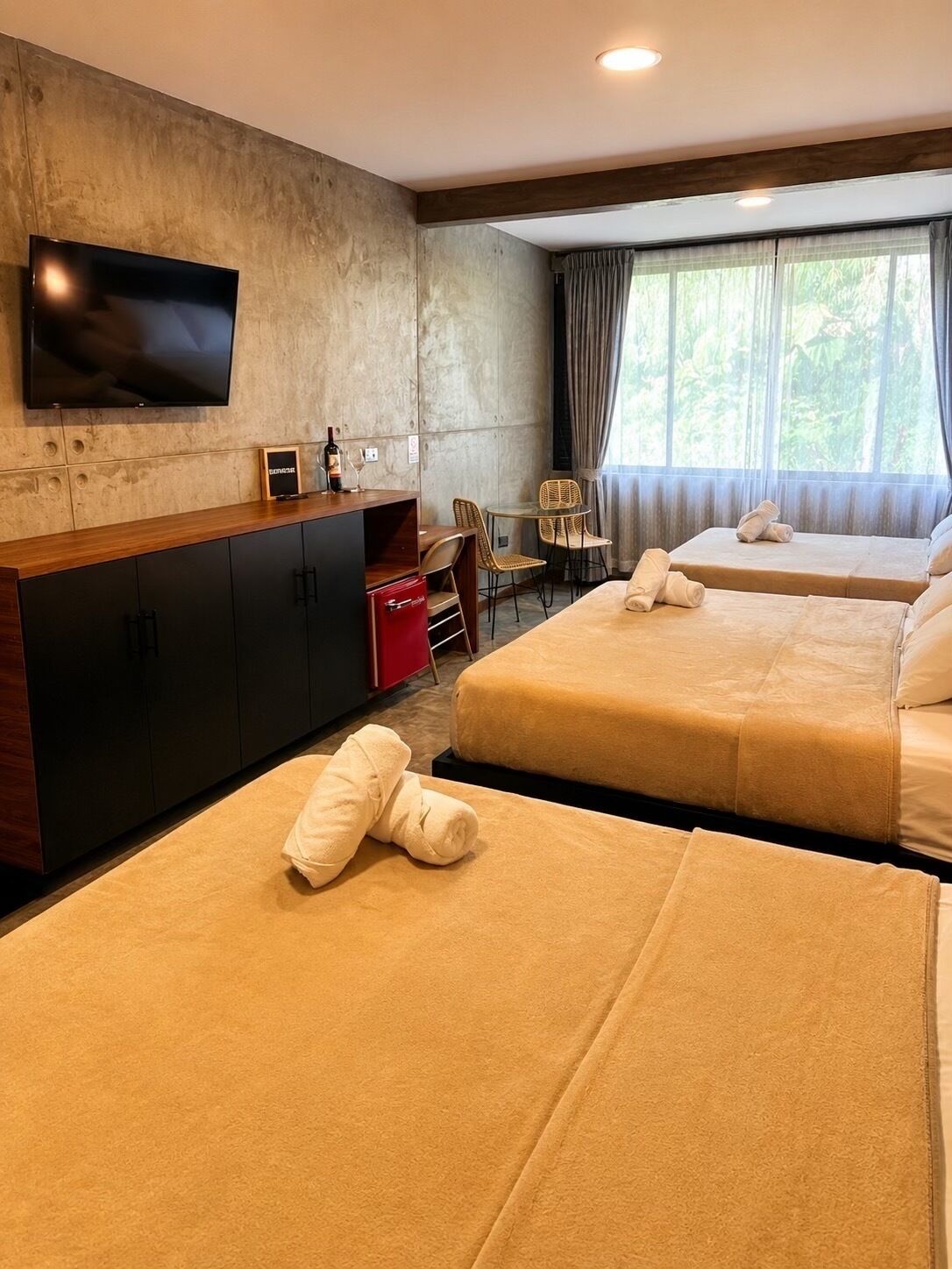 A hotel room with two beds, a TV, a minibar, and a window with curtains.