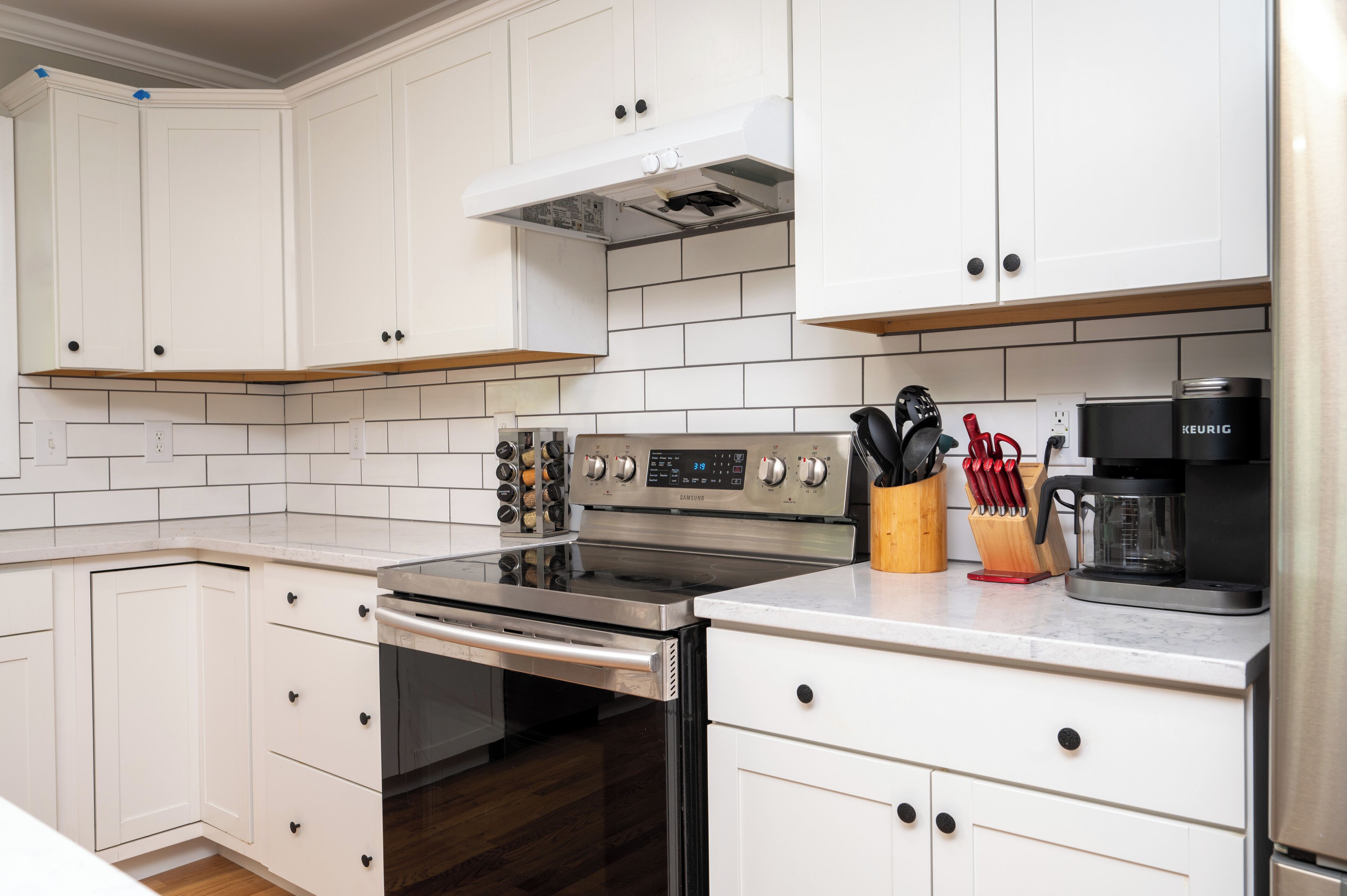A modern kitchen with white cabinetry, a stainless steel stove, and a coffee maker.
