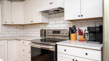A modern kitchen with white cabinetry, a stainless steel stove, and a coffee maker.