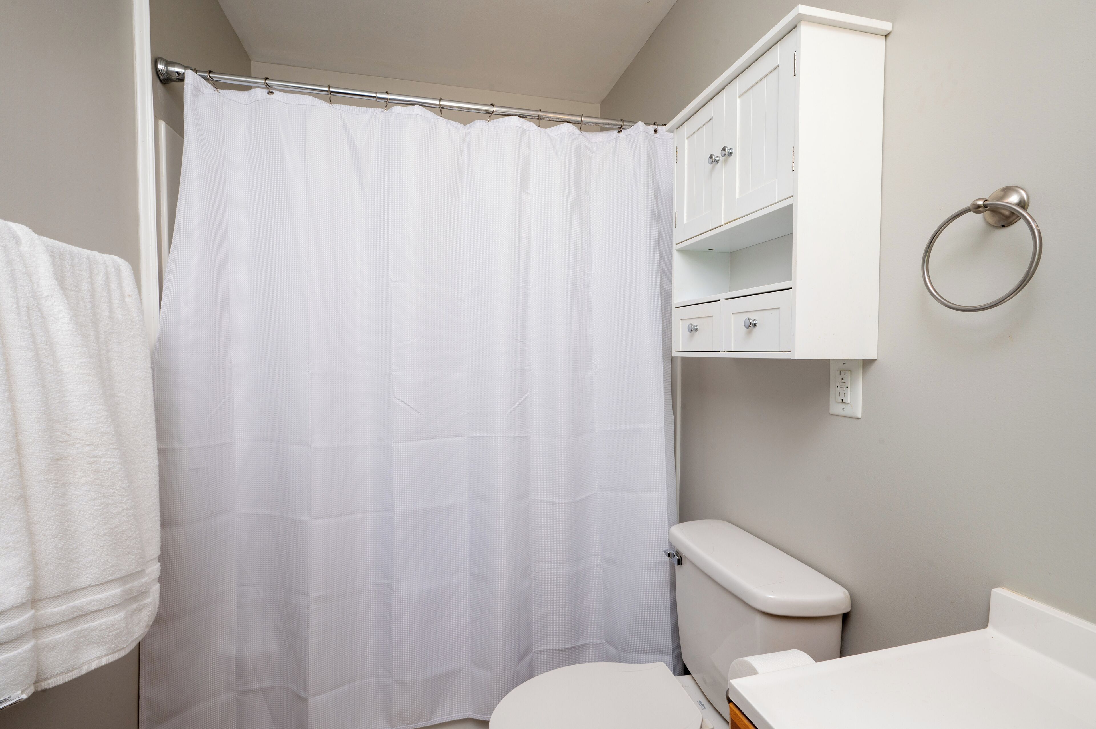 A bathroom with a shower curtain, a toilet, a sink, and a cabinet with a towel ring.