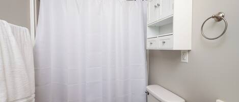 A bathroom with a shower curtain, a toilet, a sink, and a cabinet with a towel ring.