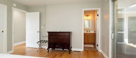 A bedroom with a wooden floor, a dark wooden dresser, a white door, and a glass sliding door leading to a balcony.