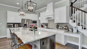 A modern kitchen with white cabinetry, a large island, stainless steel appliances, and a staircase with a wooden railing.