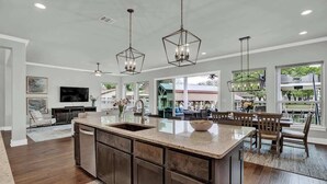A spacious kitchen with a large island, dark wood cabinets, and pendant lighting.