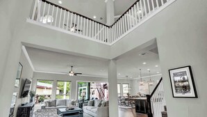 A spacious living area with a high ceiling, a staircase, and a dining area.