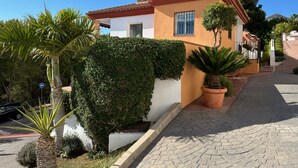 Una casa de dos pisos con techo de tejas rojas, paredes blancas y entrada con pavimento.