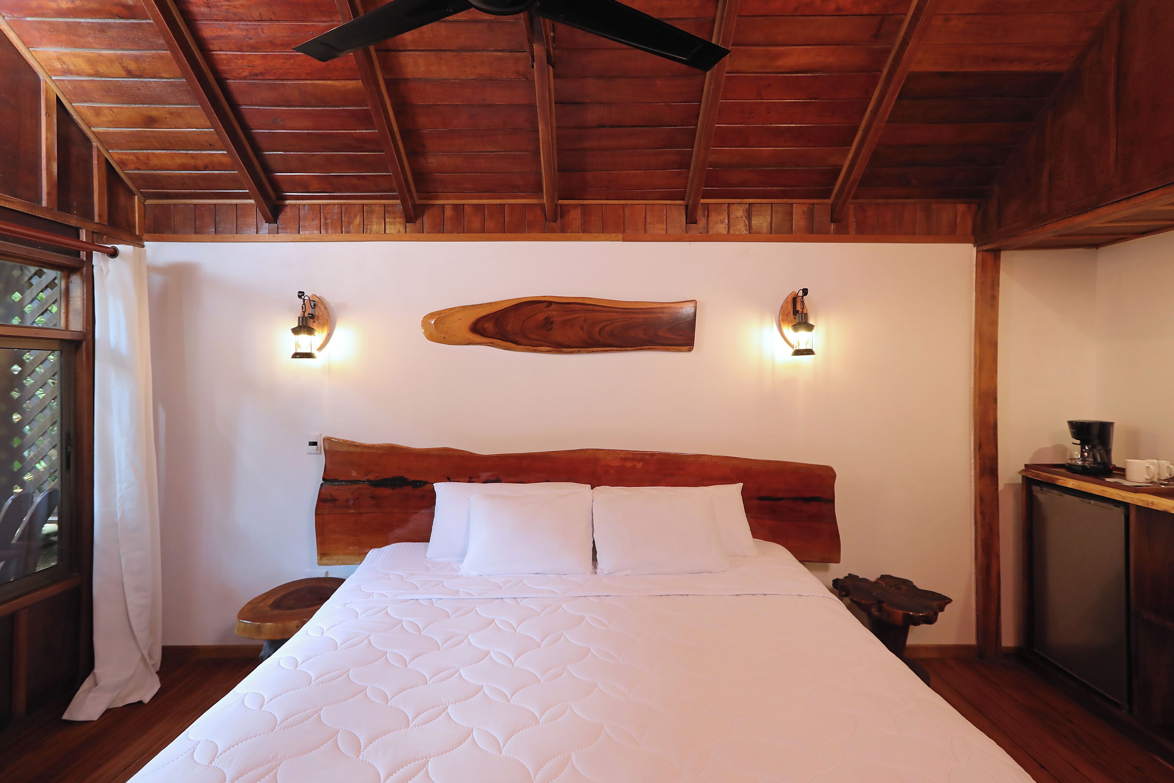 A bedroom with a wooden ceiling, a bed with white bedding, two wall-mounted lights, and a wooden headboard.