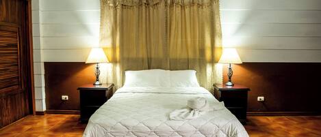 A neatly made bed with a quilted cover, two bedside lamps, and a wooden headboard.