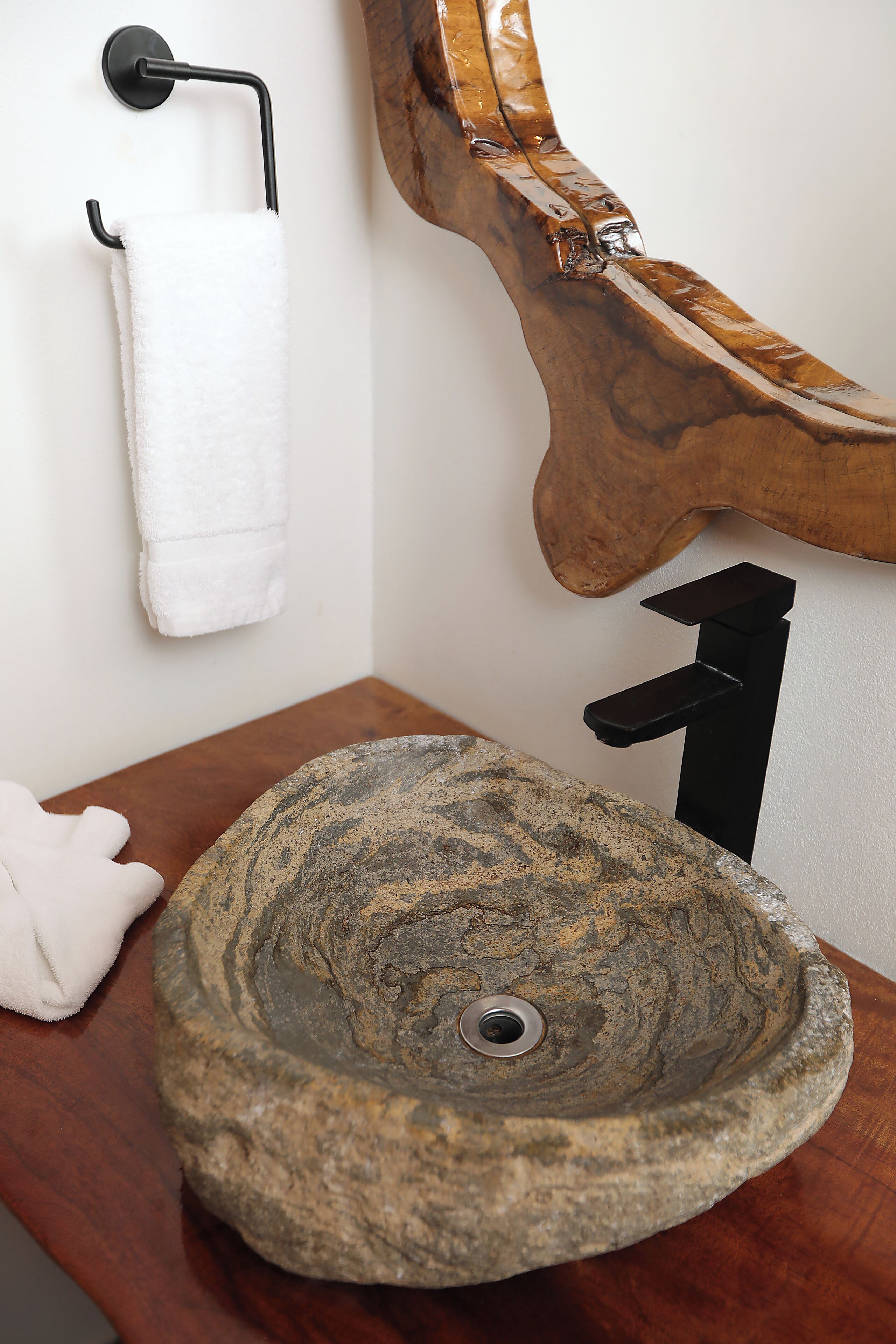 Ein Badezimmer mit einem Steinkonfett, einem hölzernen Handtuchhalter und einem weißen Handtuch.