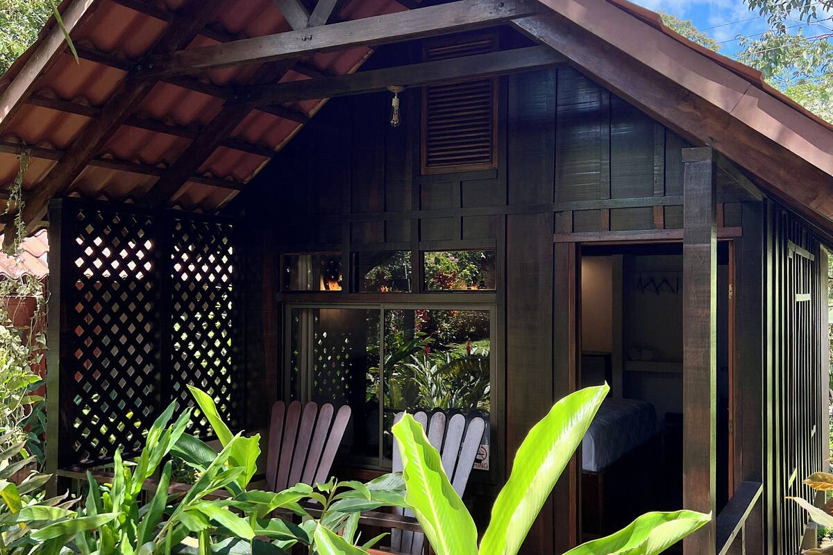 A wooden structure with a sloped roof, a covered porch, and a view of the surrounding greenery.