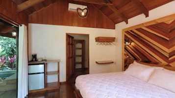 A bedroom with a wooden ceiling, a bed with white bedding, a small desk with a coffee maker, and a door leading to another room.