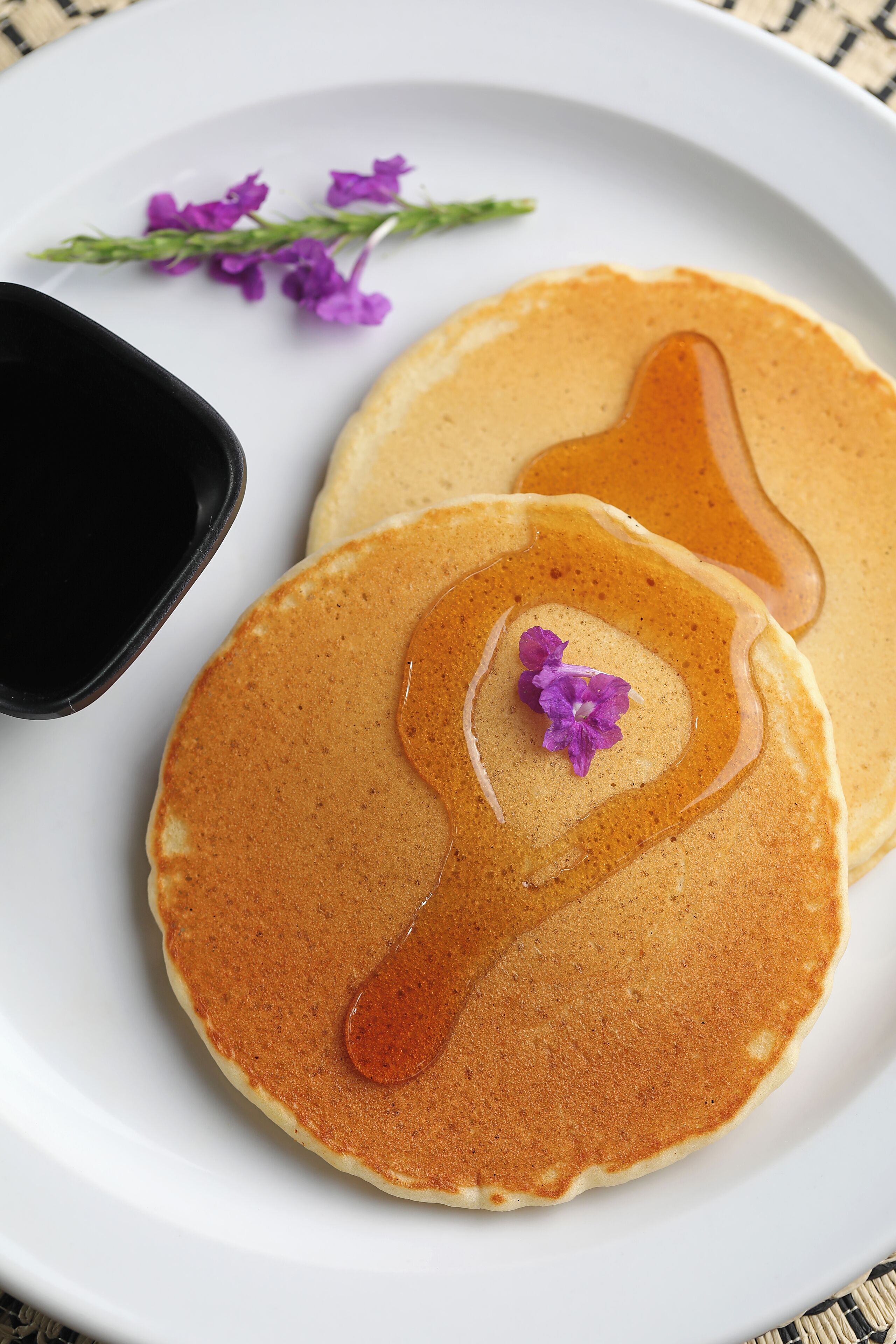 Two pancakes with syrup and a purple flower on a white plate.